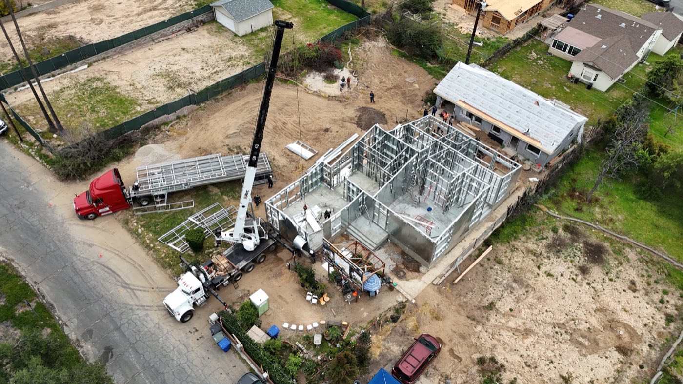 Aerial of a NAXA project site: steel delivery and framing underway on the lot